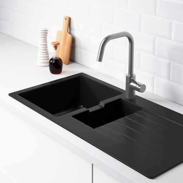 Évier de cuisine noir avec égouttoir, robinet et dosseret. Le égouttoir incliné renvoie l’eau dans la cuvette.