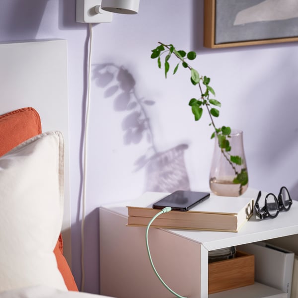 Table de chevet de chambre avec livres, téléphone, vase et verres.