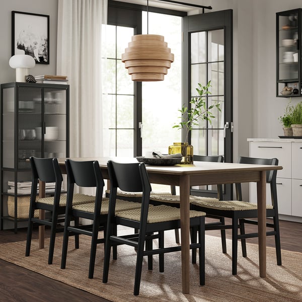 Ensemble de table extensible moderne, chaises tressées, tapis élégant, suspension, étagères avec des plantes et des livres.