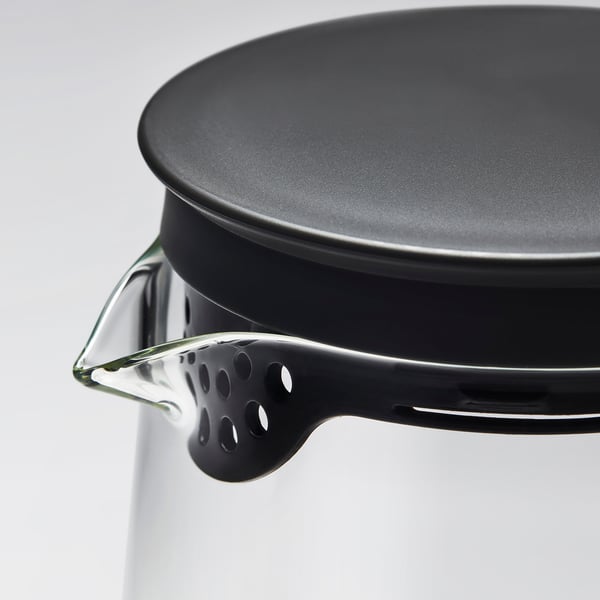 Gros plan d’un pichet en verre robuste avec couvercle à passoire, montrant des matériaux et un design de haute qualité.