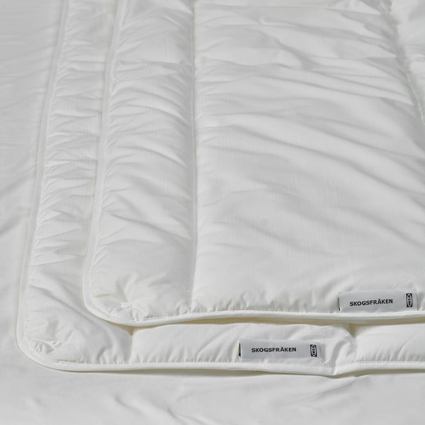 Couette blanche et propre sur le lit, mettant en valeur un tissu de qualité et un savoir-faire artisanal, avec des étiquettes de marque SKOGSFRÄKEN visibles et le logo IKEA.