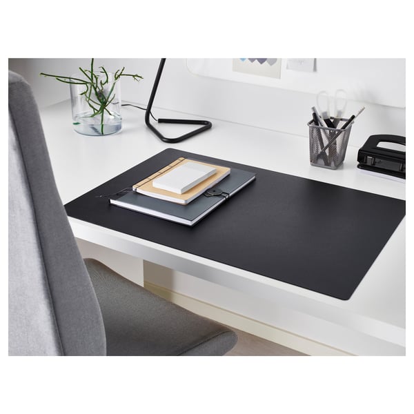 Espace de travail moderne avec sous-main SKRUTT noir, cahiers, porte-stylo et petite plante. Le coussin couvre le bureau, a une surface lisse.