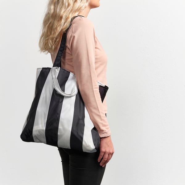 Femme tenant un sac noir et argenté, probablement le SKYNKE, conçu pour être léger et polyvalent pour le shopping ou les voyages.