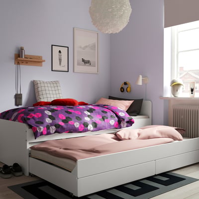 Chambre moderne avec lit SLÄKT, literie colorée, lit gigogne. Murs violets, art, tapis, lampe, écouteurs.