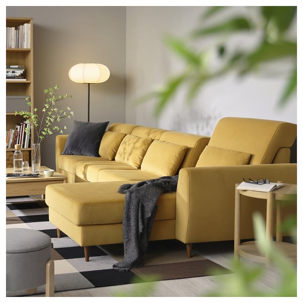 Salon moderne avec canapé sectionnel SLATORP jaune, couverture noire, oreillers bleus, table basse en bois, grande lampe et plantes.