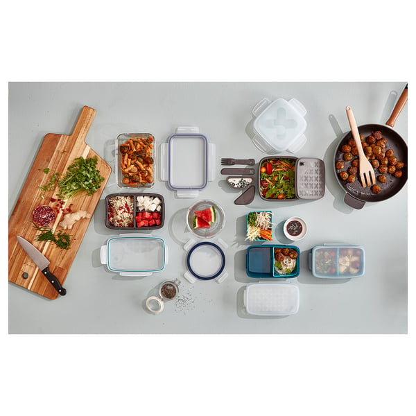 Vue de dessus d’une planche à découper en bois, de divers produits alimentaires et de récipients en plastique colorés de différentes tailles.
