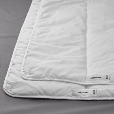 Couette blanche sur lit gris, bordée d’une étiquette en matière recyclée, mettant en valeur la qualité et le confort.