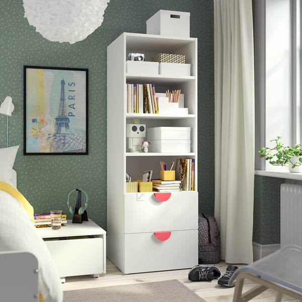 Bibliothèque blanche dans la chambre avec livres, décoration et affiche de paris. Murs à motifs verts, fenêtre avec rideaux.