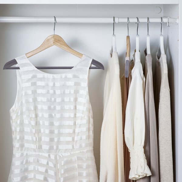 Placard avec cintres en bois. Le cintre gauche contient une robe blanche sans manches. La section droite contient plusieurs vêtements de couleur claire.