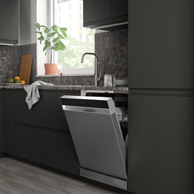 Cuisine moderne sombre avec un lave-vaisselle SÖDERBODA ouvert, plus petit que les armoires environnantes, près d’une fenêtre avec une plante.