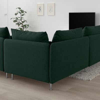 Canapé sectionnel vert foncé SÖDERHAMN avec des assises profondes, posé contre des murs blancs, à côté d’une plante et d’une télévision, sur un sol en bois clair.