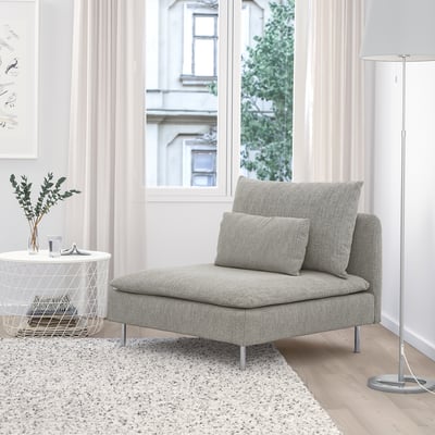 Chaise grise SÖDERHAMN, basse et douce avec textile d’élite. Petite table d’appoint, lampadaire et art à proximité. Une grande fenêtre montre un bâtiment.