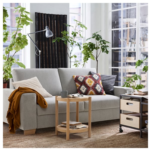 Salon moderne avec un canapé SÖRVALLEN gris clair, un coussin coloré, une table d’appoint en bois et des plantes d’intérieur.