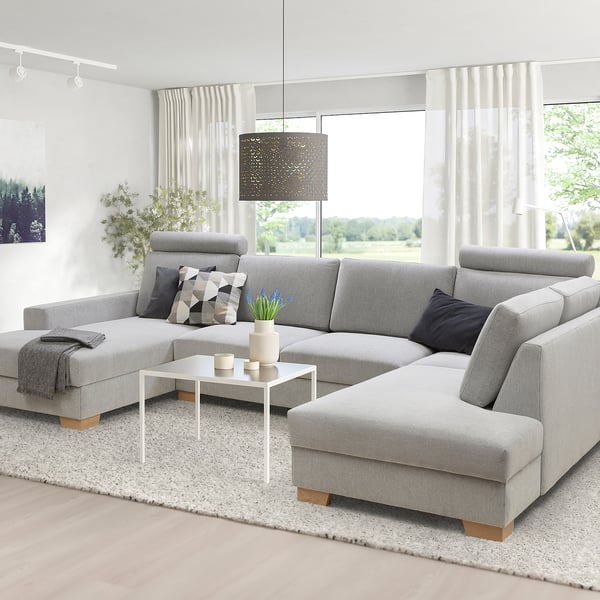 Canapé sectionnel SÖRVALLEN gris dans le salon, avec coussins, couverture, table basse et grandes fenêtres.