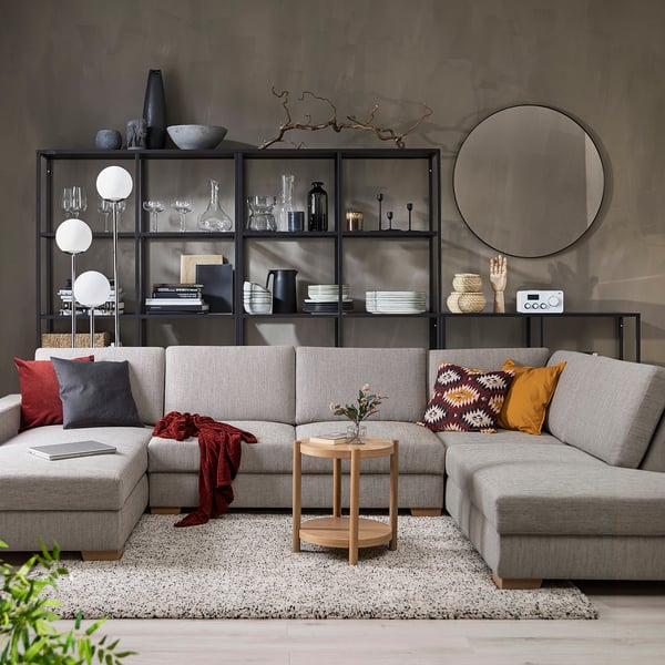 Salon moderne avec des sectionnels SÖRVALLEN gris, des coussins colorés, une table basse en bois et des étagères noires avec des objets décoratifs.