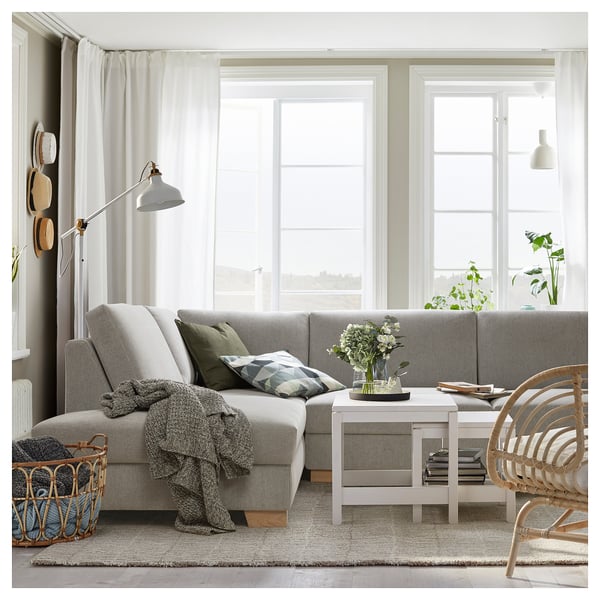 Salon moderne avec canapé gris clair SÖRVALLEN, table basse blanche, panier en bois, grande fenêtre, rideaux, lampe, plantes et matériaux naturels.