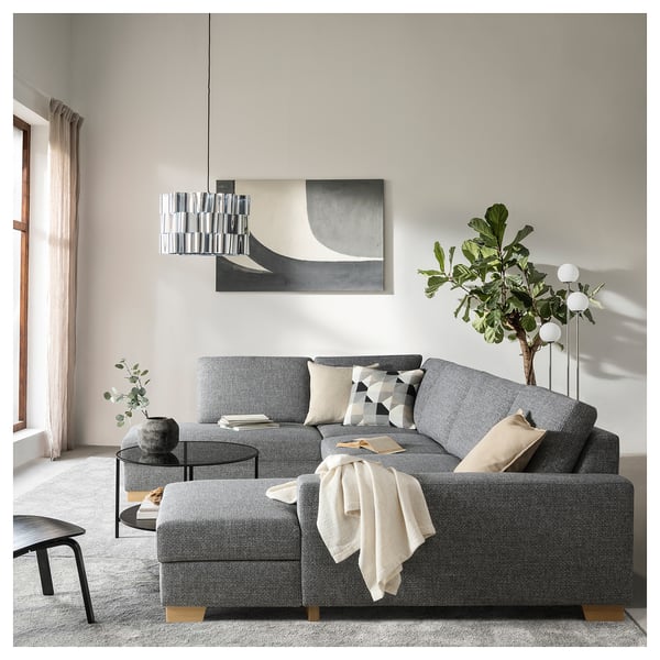 Salon moderne avec canapé gris SÖRVALLEN, coussins géométriques, table basse en verre, lampe suspendue, grand tableau et plante d’intérieur verte.