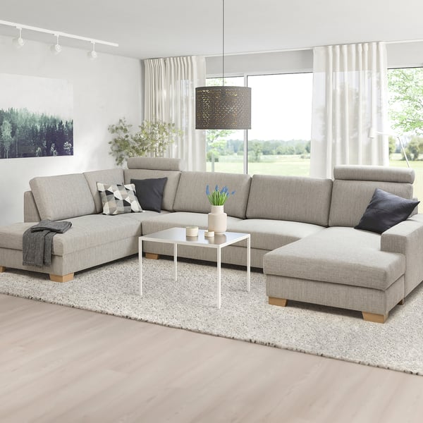 Canapé moderne en forme de L avec des couleurs neutres, design minimaliste, pieds en bois, près de la fenêtre, avec tapis et coussins.