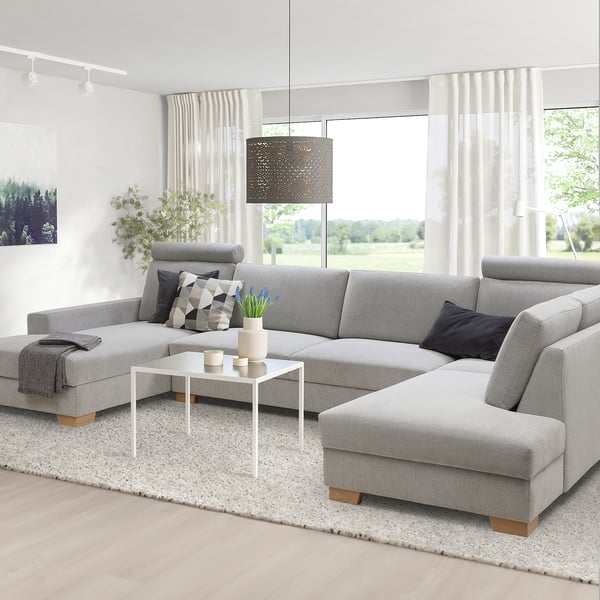 Canapé sectionnel gris moderne avec chaise, grandes fenêtres, table basse, plantes, lampe, tapis.