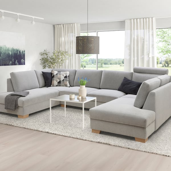 Canapé moderne gris en forme de U, grand, avec chaise longue, oreillers noirs et blancs, table basse, rideaux blancs, lumière naturelle.