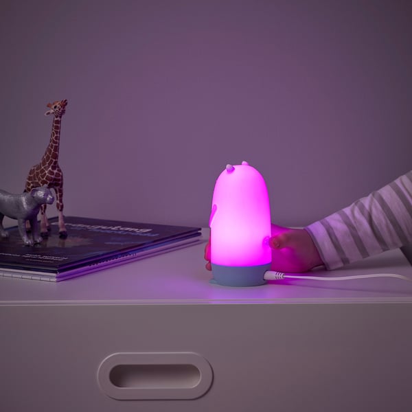 Main d’enfant avec veilleuse loutre rose. Brille, change de couleur, près des jouets et des livres.