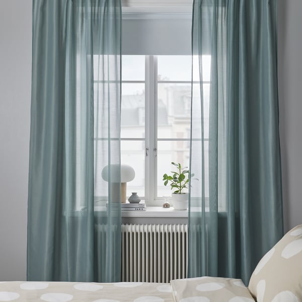 Des rideaux turquoise encadrent la fenêtre sur le radiateur avec plante et lampe.