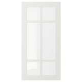 Une porte d’armoire STENSUND blanche avec un panneau de verre divisé en quatre sections par des cadres en bois, conçue pour une utilisation en cuisine.