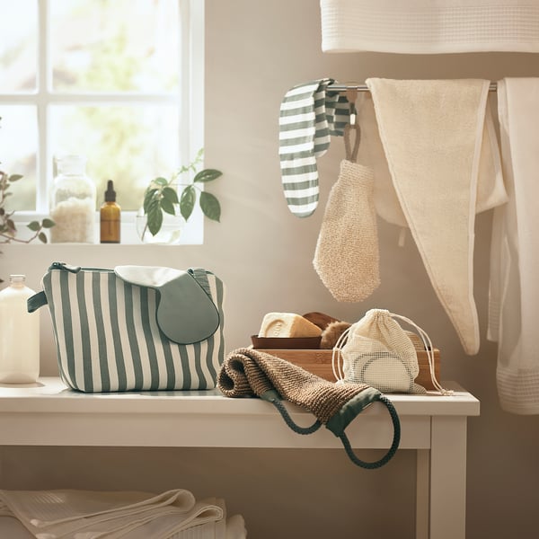 Scène de salle de bain avec sac à main rayé vert/blanc, serviettes blanches et serviette à cheveux suspendue. Fenêtre avec plante.