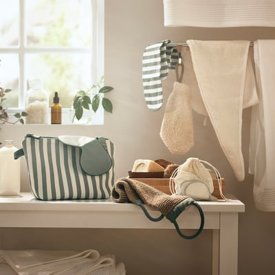Scène de salle de bain avec sac à main rayé vert/blanc, serviettes blanches et serviette à cheveux suspendue. Fenêtre avec plante.