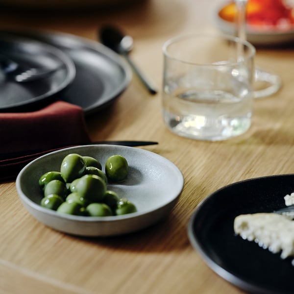 Petit bol de pois vert vif sur une assiette grise, un verre d’eau claire et un petit plat avec de la nourriture blanche et friable à côté d’eux sur une table en bois.