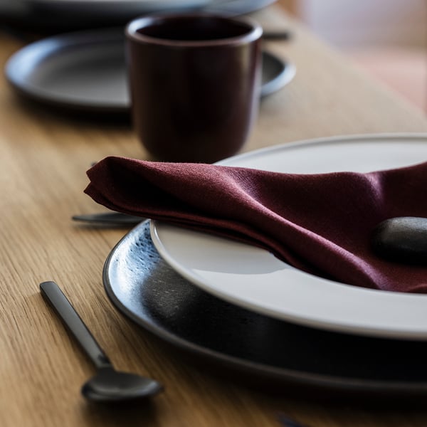 Dressage de table élégant avec serviette en lin foncé, assiette blanche et couverts noirs sur une table en bois, reflétant une qualité supérieure et un design élégant.