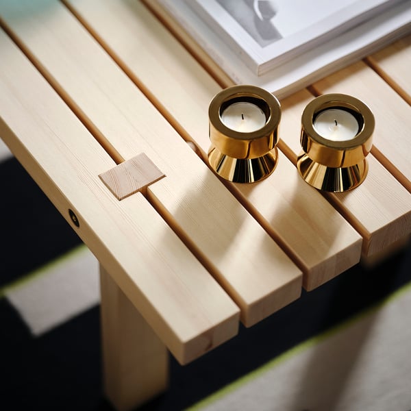 Un banc en bois minimaliste avec des bougeoirs dorés dessus. Fabriqué à partir de bois de couleur claire, il présente des détails de design élégants et une finition de haute qualité.