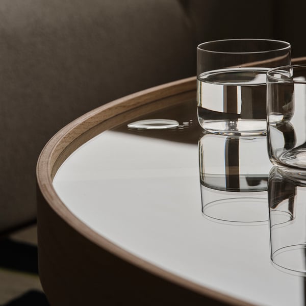 Table ronde en verre avec bord en bois, contenant trois verres transparents, réfléchissant la lumière.