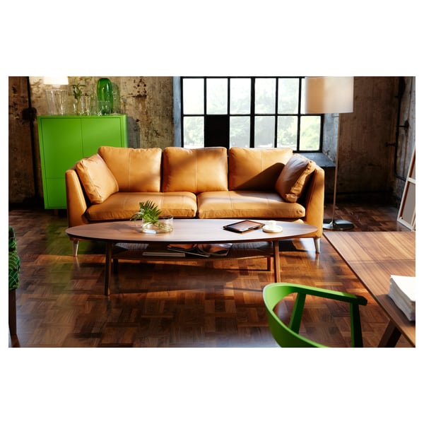 Un salon moderne avec un canapé en cuir marron, une table basse en bois ovale foncé avec une étagère et des objets de décoration verts, notamment une armoire et une chaise.