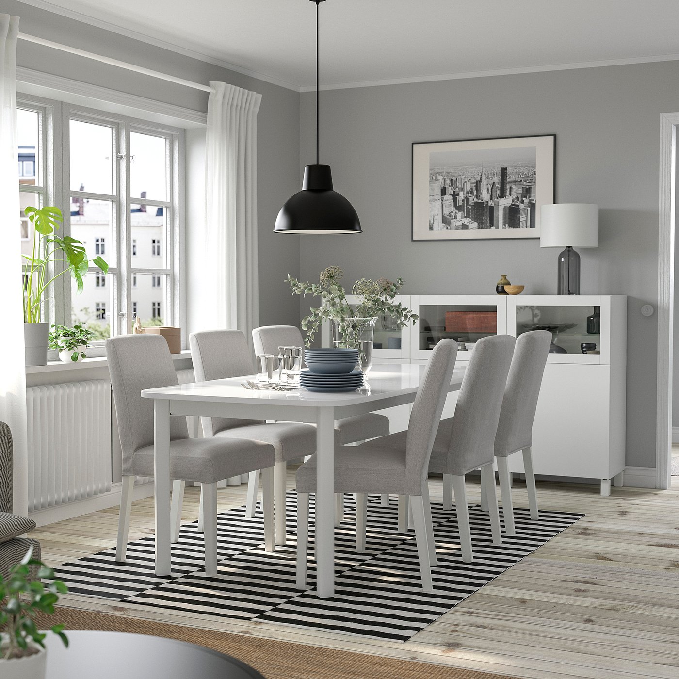 Salle à manger moderne avec table extensible pour six personnes, lampe noire, tapis rayé, fenêtre avec vue sur la ville.