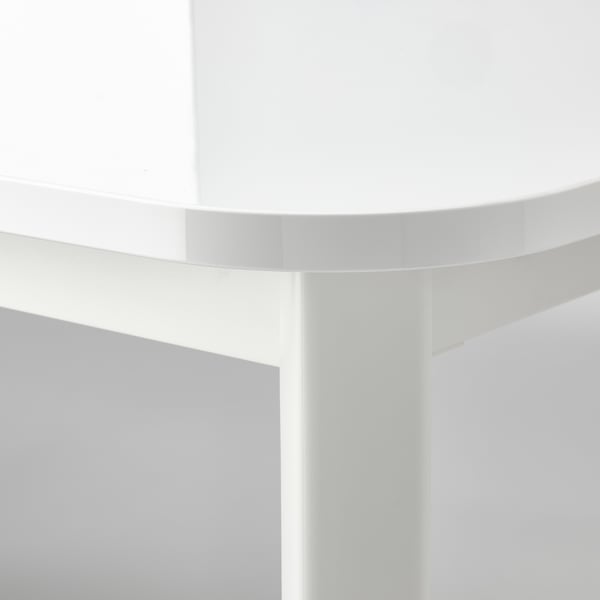 Gros plan du bord de la table STRANDTORP, présentant une finition blanche lisse et durable et un support de pieds en acier robuste.
