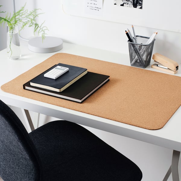 Sous-main en liège beige sur bureau blanc, avec cahiers, fougère, porte-plume et agrafeuse.