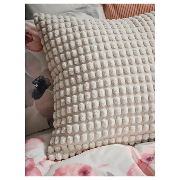 Oreiller blanc cassé avec un motif circulaire texturé sur un lit, mettant en valeur la housse de coussin SVARTPOPPEL en polyester recyclé.