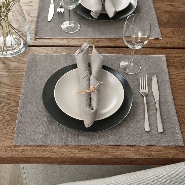 Set de table avec sets de table gris SVARTSENAP, assiettes à bord noir, serviettes pliées, argenterie et verre à vin.