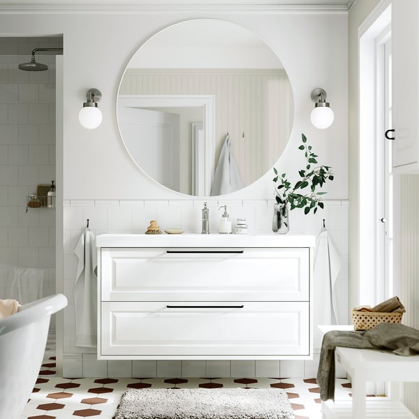 Salle de bains élégante avec meuble-lavabo TÄNNFORSEN, miroir et tiroirs. Carrelage blanc, sol à motifs, plantes vertes. Mélange moderne et classique.