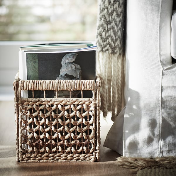 Panier en osier avec des livres sur le siège, des textiles doux à côté, un décor naturel et terreux.