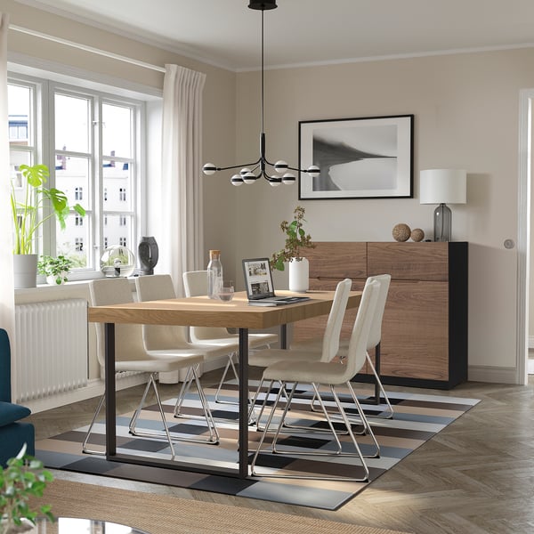 Table à manger extensible en chêne pour 6-8 personnes, avec base en métal et tapis rayé. Chaises légères, grande fenêtre et suspension dans une pièce minimaliste.