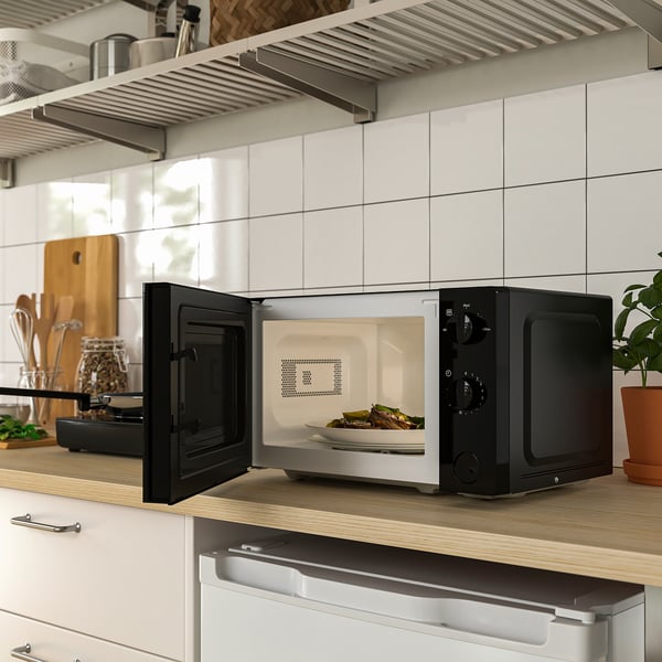 Micro-ondes noir et argent sur le comptoir, les portes s’ouvrent révélant la nourriture à l’intérieur.