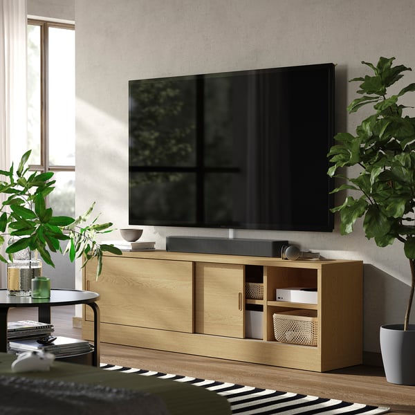 Grand meuble TV TONSTAD avec finition en bois lisse, avec portes coulissantes et étagères ouvertes, positionné contre un mur avec une télévision à écran plat sur le dessus.