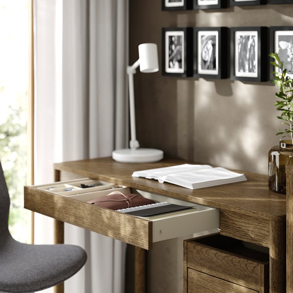Bureau en bois avec un tiroir ouvert, contenant des cahiers et une lampe sur le dessus.