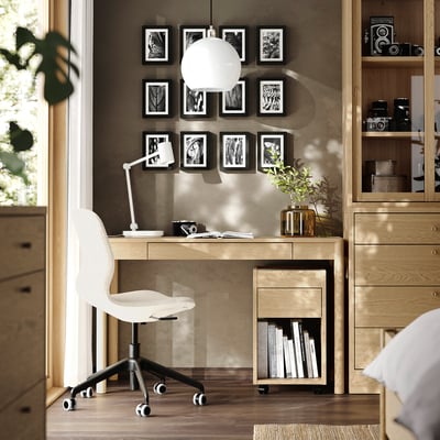 Bureau à domicile moderne avec bureau en chêne TONSTAD, chaise blanche, photos et lampe globe. La lumière naturelle remplit la pièce.