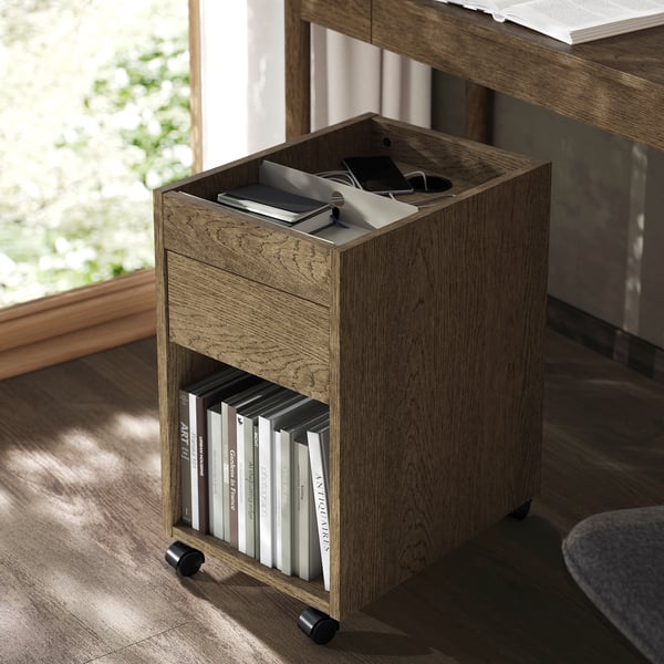 Unité de rangement mobile en bois avec tiroir et étagère, contenant des livres et des articles de bureau. Idéal pour les petits espaces.