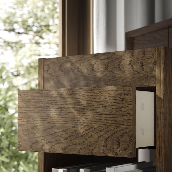 Meuble à tiroirs en bois foncé au design moderne et aux tiroirs à fermeture douce, positionné près d’une fenêtre avec vue extérieure verdoyante.