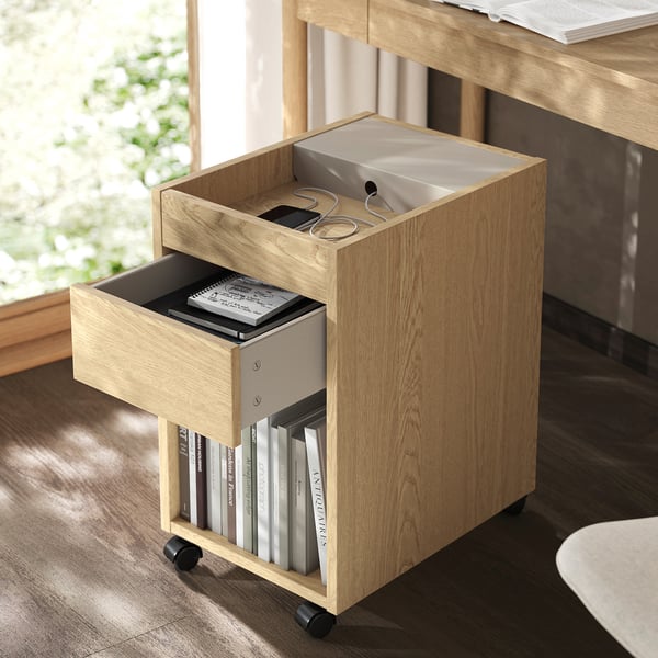 Meuble à tiroirs mobile en bois avec étagère ouverte. Contient des livres, des cahiers et de petits objets de manière élégante.