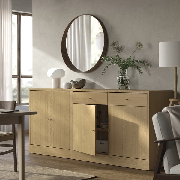Salon moderne : buffet en bois, miroir rond, lampe blanche, chaise, fleurs.